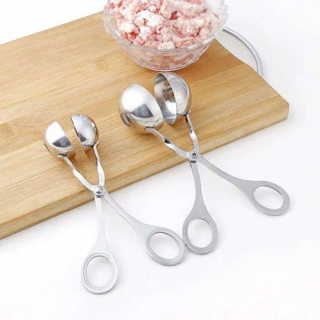 Two pairs of metal meatball scoops next to a bowl of ground meat on a wooden board.