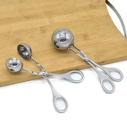 Two stainless steel meatball scoops on a wood cutting board.