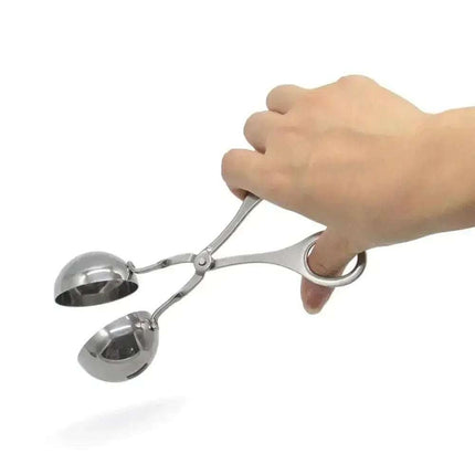 A person's hand holds a pair of silver-colored, metal meatball tongs.