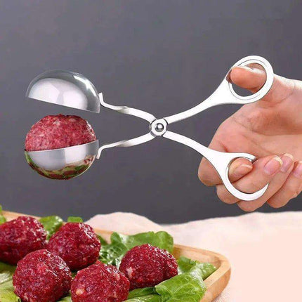 A pair of silver metal meatball-making tongs holding a meatball over a platter of meatballs on green lettuce.